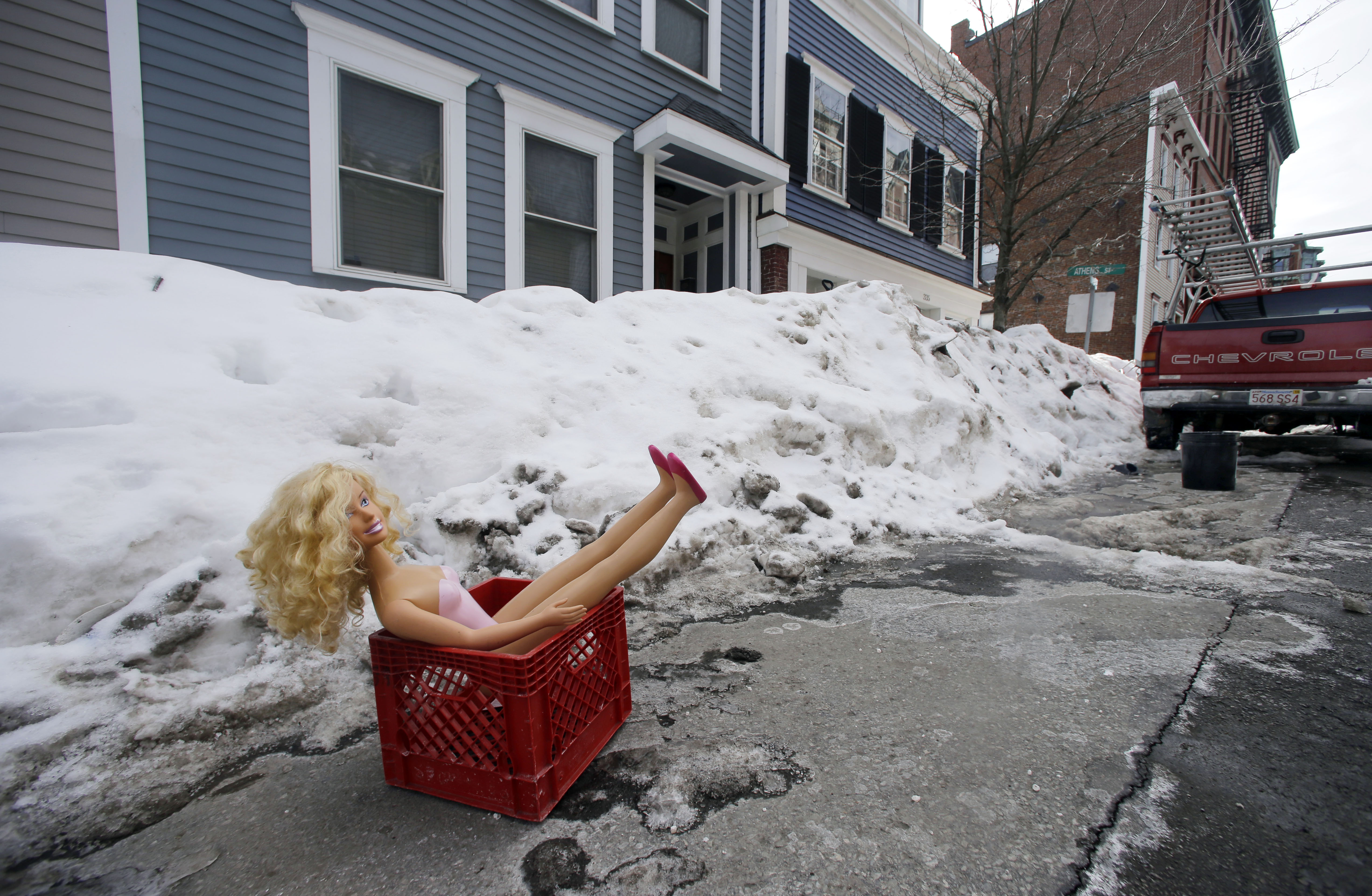 In this Feb. 23, 2015 photo, a fashion doll in a milk crate saves a parking space on a residential street in South Boston. Officials typically turn a blind eye to the lawn chairs, orange cones and assorted bric-a-brac Bostonians use to reserve a parking space after clearing it of snow. That ends Monday, March 2, 2015, with an order from City Hall to remove space savers, reigniting the ugly parking wars that have pitted neighbor against neighbor. (AP Photo/Elise Amendola)