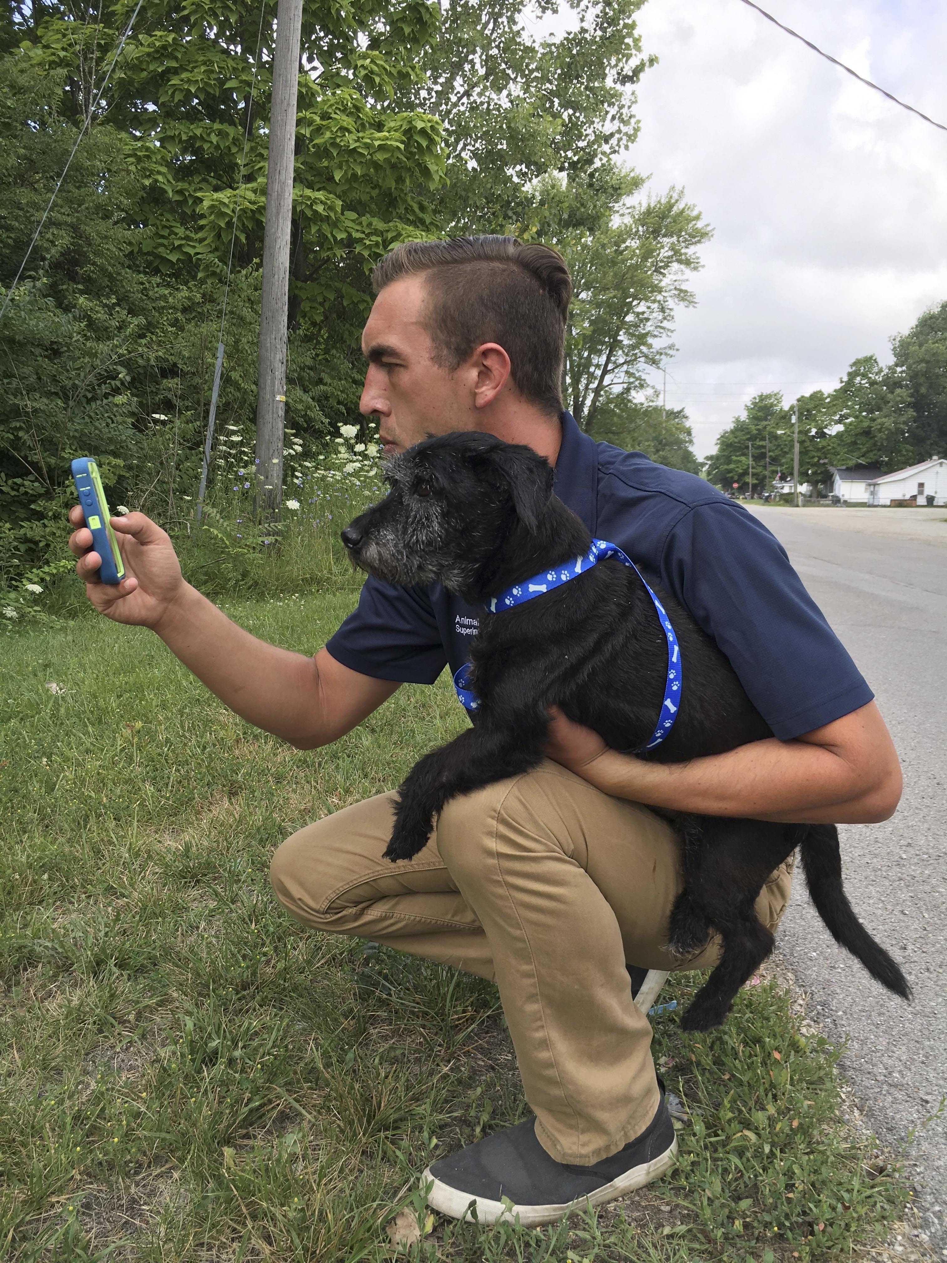 In this Wednesday, July 13, 2016, photo, provided by the Muncie Animal Shelter in Muncie, Ind., shelter superintendent Phil Peckinpaugh holds a terrier mix as he plays “Pokemon Go” in Muncie, Ind. Peckinpaugh came up with the idea of asking "Pokemon Go" players to walk an adoptable dog as they wander the streets of the eastern Indiana city doing battle with digital monsters on their smartphones. (Phil Peckinpaugh/Muncie Animal Shelter via AP)