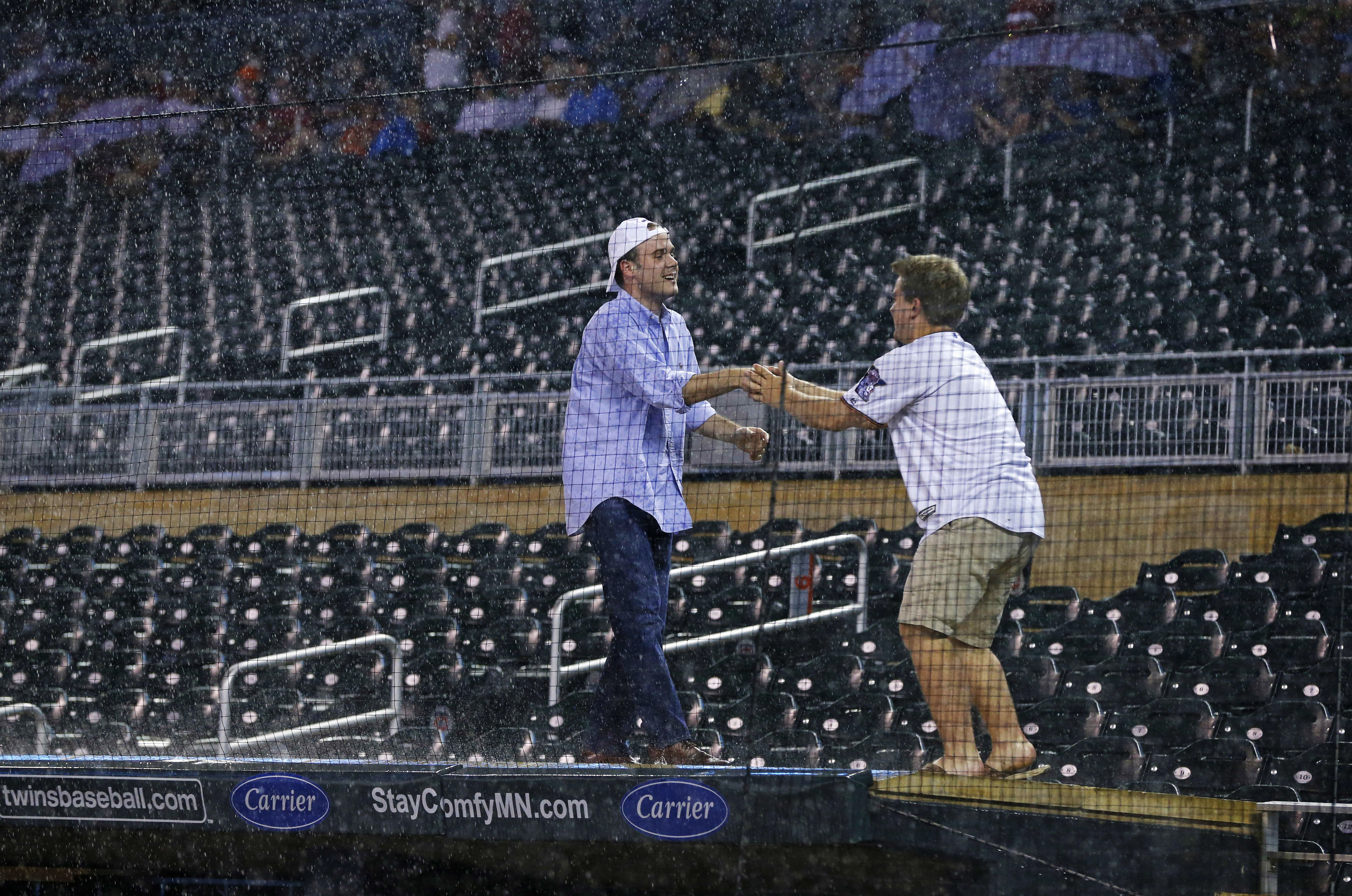 Two fans ignore the rain delay and celebrate atop the Minnesota Twins dugout during a rain delay in a baseball game against the Houston Astros Wednesday, Aug. 10, 2016 in Minneapolis. The Houston-Minnesota game was postponed Wednesday by persistent rain that started in the third inning and was forecast to last throughout the night. (AP Photo/Jim Mone)