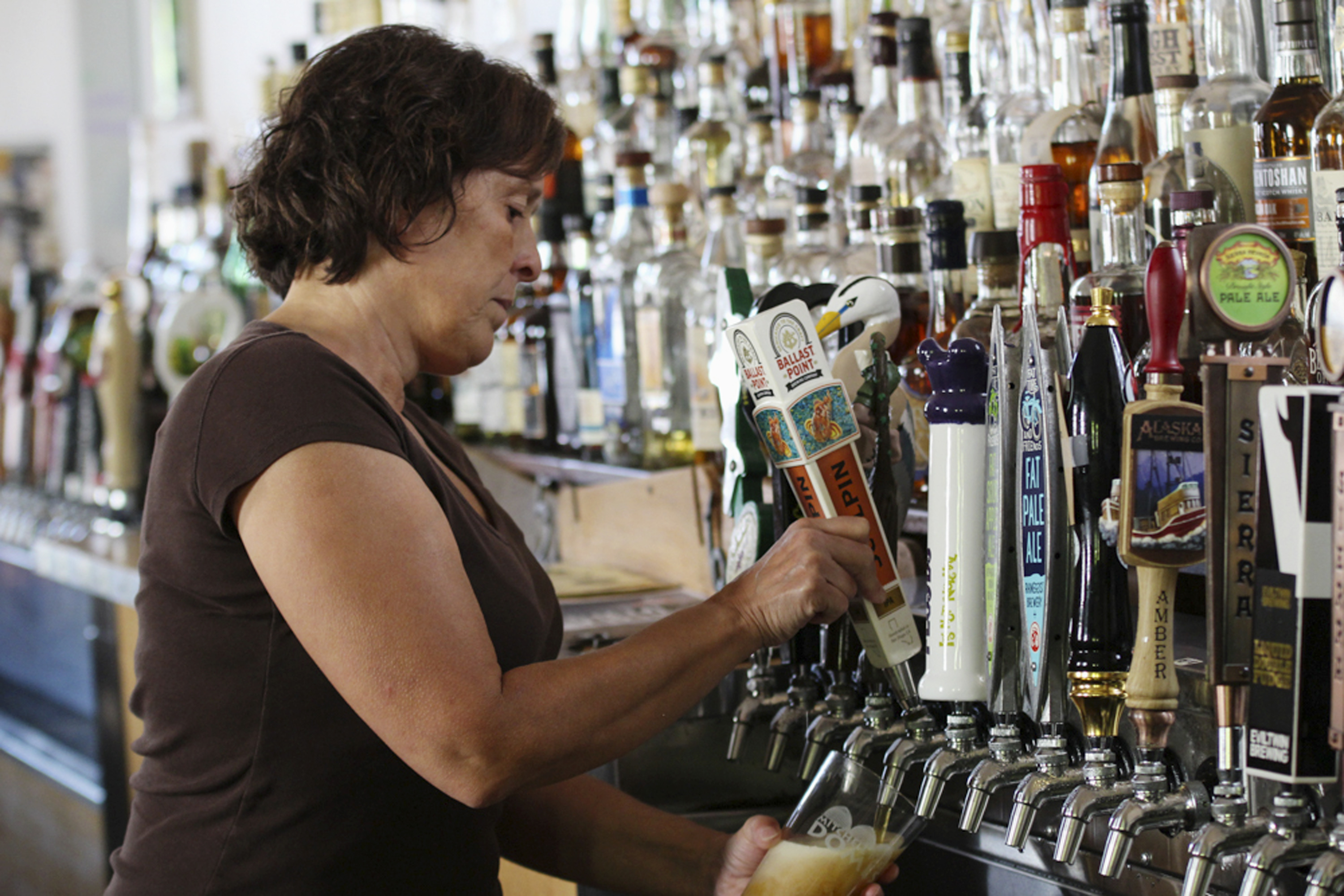 In this July 21, 2016, photo, bartender Catherine Pierluissi pulls a Ballast Point tap handle at Sugar Maple in Milwaukee, where there are at least 60 beers on tap. The number of craft breweries has more than doubled in the last five years, making tap handles that go in bars to promote their beers big business. AJS Tap Handles in Random Lake, Wis., is one of the largest makers of tap handles in the nation and made Ballast Point handle, among others at the bar. (AP Photo/Carrie Antlfinger)